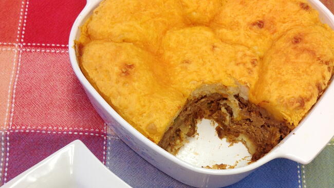 Beef and biscuit casserole in a white dish, on a multi-colored table cloth