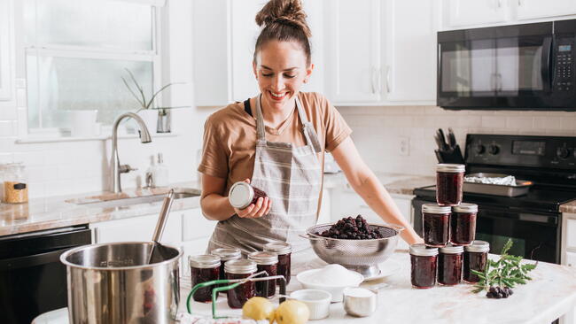 woman in kitchen making jam using the water-bath canning method with a stainless steel stock pot